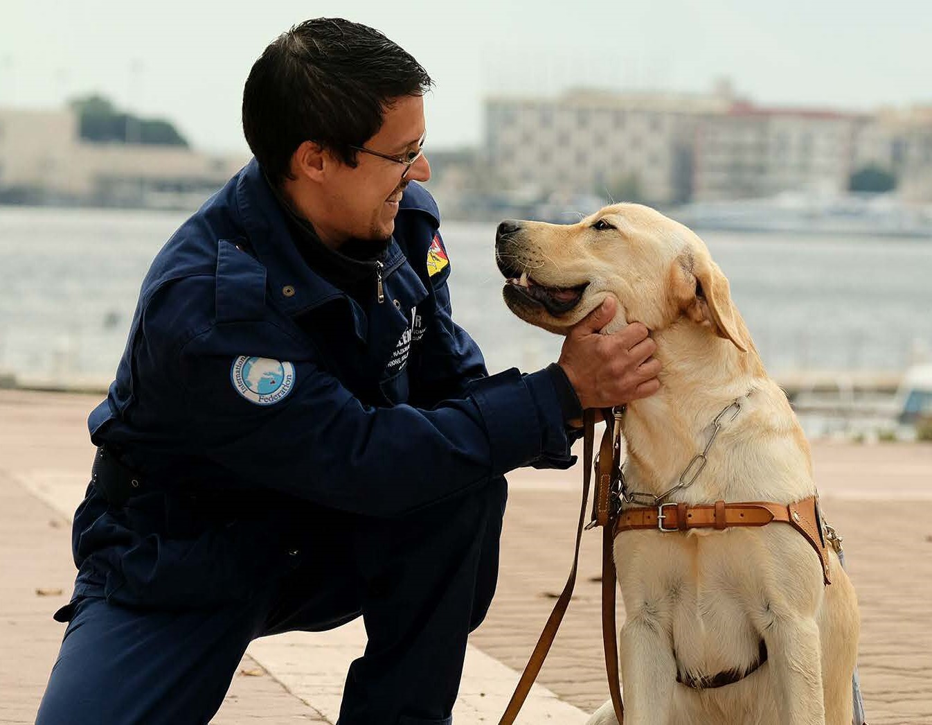 Nell’immagine un istruttore che coccola un cane da guida.